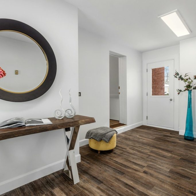 A modern hallway with a round mirror, a console table, and a blue vase. completed with a stunning dark wood LVT